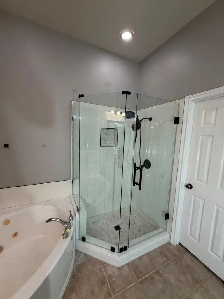 Neo-angle glass shower we built beside an existing corner tub, with a pebble mosaic floor, tiled niche and matte black fixtures.