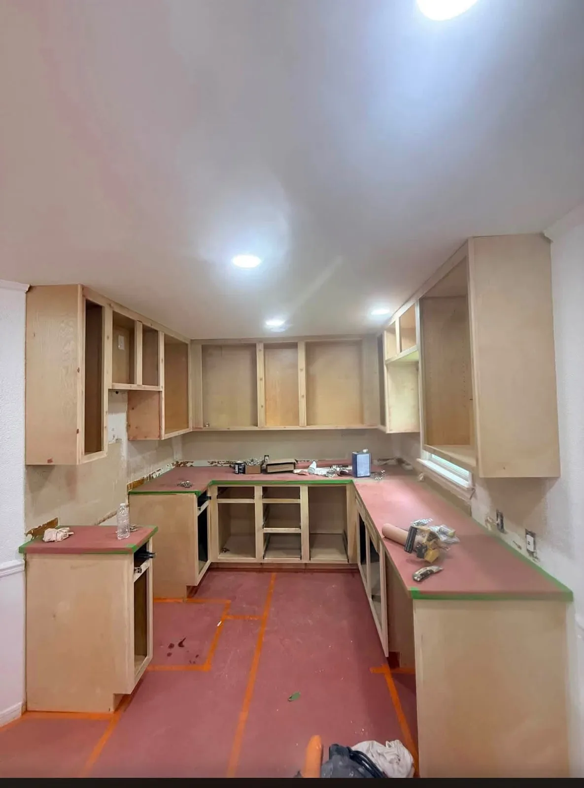 The same kind of kitchen mid-job: new cabinet boxes hung and leveled, counters masked, floor papered and taped before doors and tops go on.